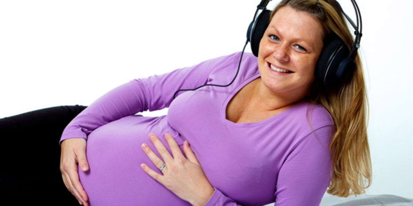 Schwangere Frau, halb liegend, hört Musik über Kopfhörer.