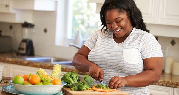 Jüngere, übergewichtige Frau, schneidet Gemüse klein.
