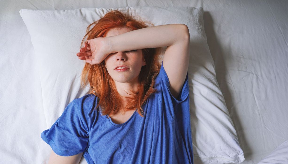 Junge Frau, liegt müde im Bett.