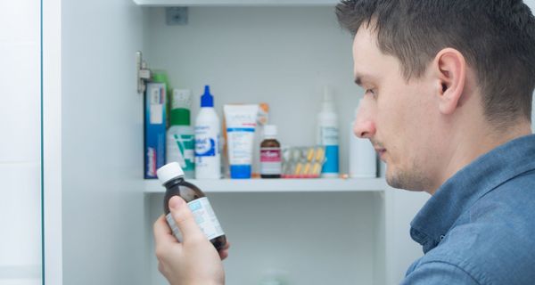 Man betrachtet ein Medikament vor seinem Arzneischrank.