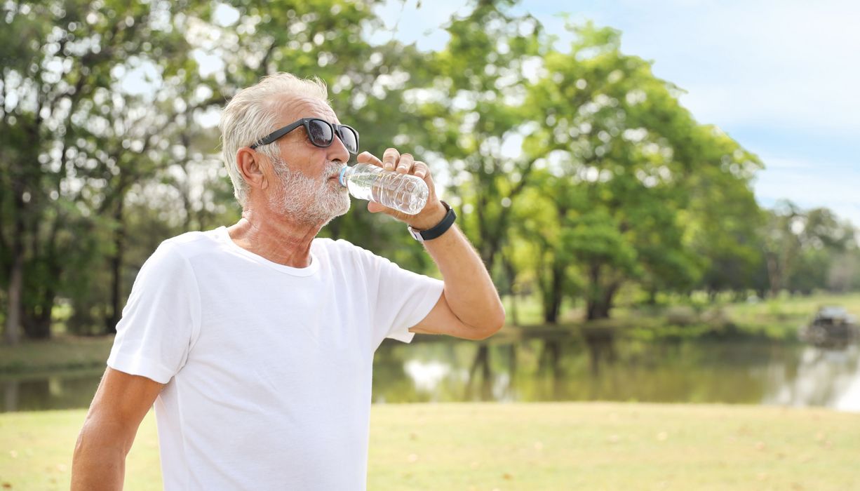 Älterer Mann mit Sonnenbrille trinkt aus einer Flasche Wasser.