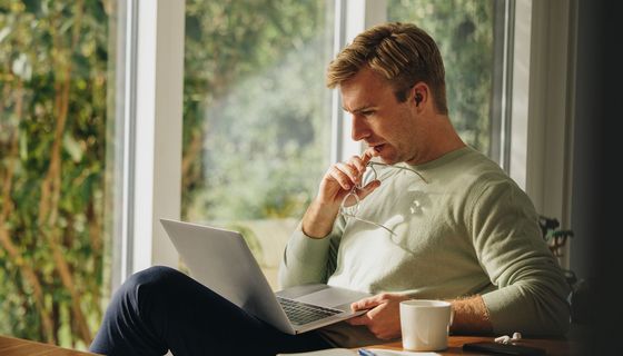 Mann blickt nachdenklich auf den Laptop auf seinem Schoß.