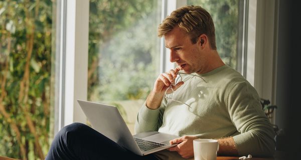 Mann blickt nachdenklich auf den Laptop auf seinem Schoß.