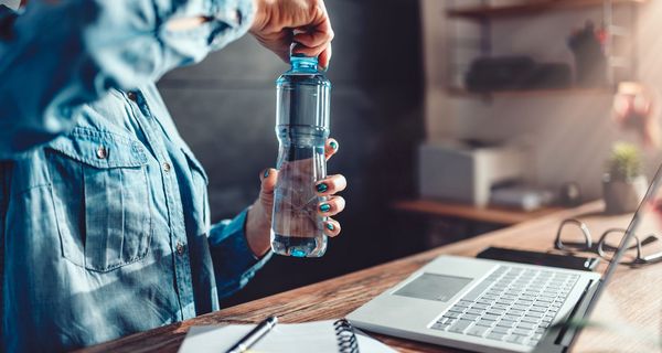 Frau öffnet Trinkflasche im Büro.