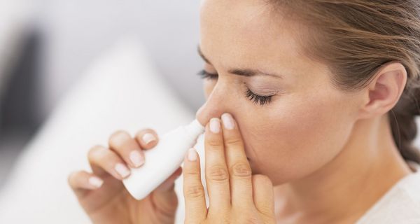 Frau sprüht sich Nasenspray in die Nase.