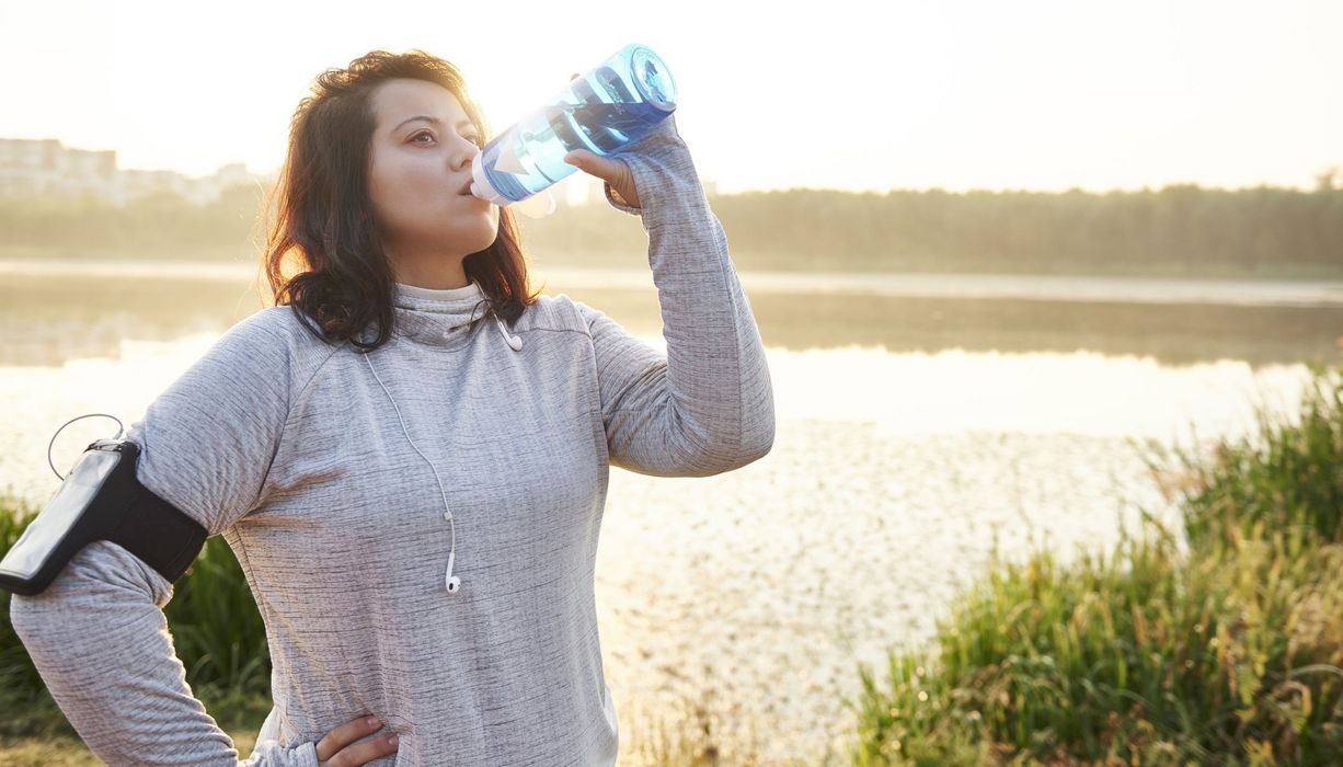 Übergewichtige Frau in Sportkleidung, trinkt Wasser.