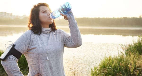 Übergewichtige Frau in Sportkleidung, trinkt Wasser.