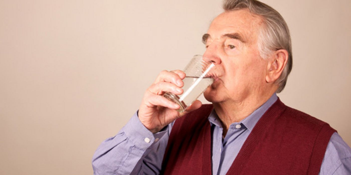 Älterer Mann trinkt ein Glas Wasser.