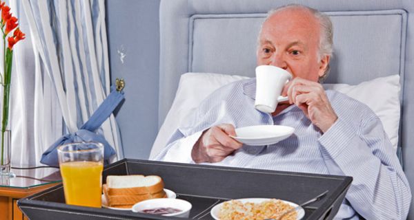 Älterer Mann frühstückt im Krankenhausbett.