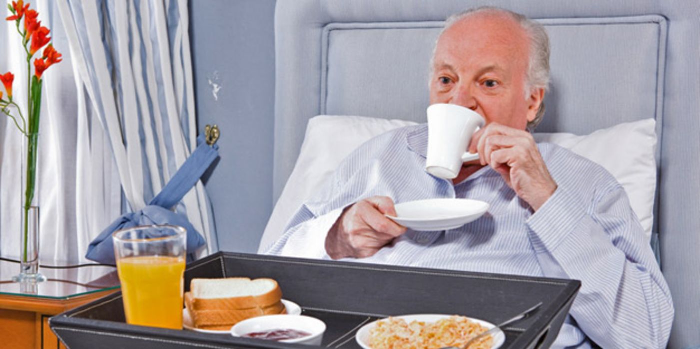 Älterer Mann frühstückt im Krankenhausbett.