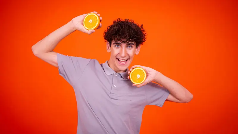Gut gelaunter junger Mann mit zwei halben Orangen.