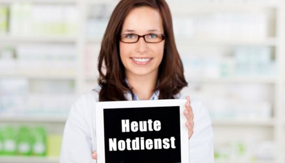 Apothekerin hält ein Schild mit der Aufschrift "Heute Notdienst" in die Kamera