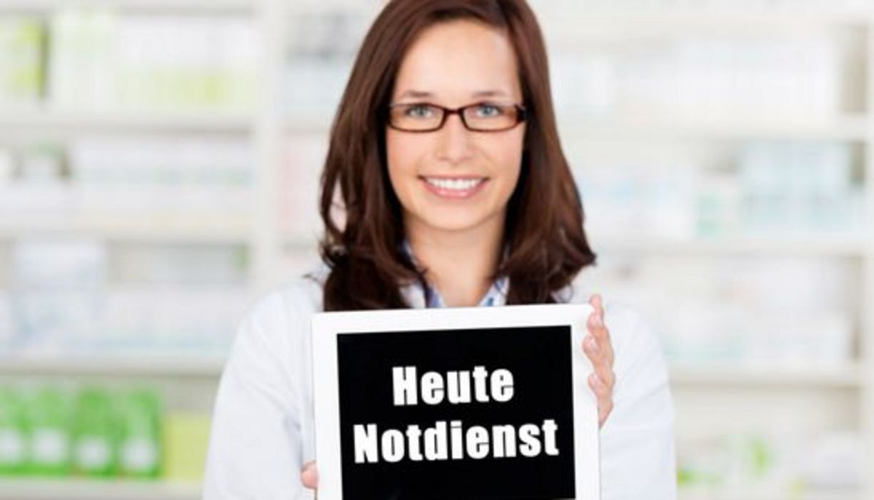 Apothekerin hält ein Schild mit der Aufschrift "Heute Notdienst" in die Kamera