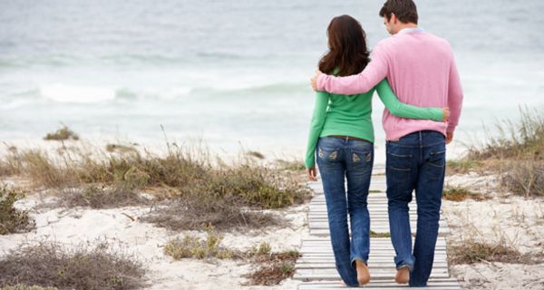 Junges Paar läuft einen Weg in den Dünen entlang aufs Meer zu