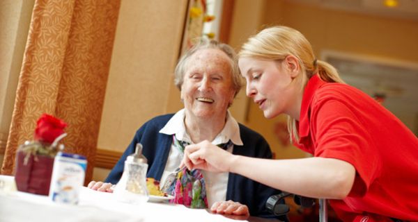 Pflegerin macht mit einer Gabel einer pflegebedürftigen Seniorin ein Stück von einem Kuchen ab