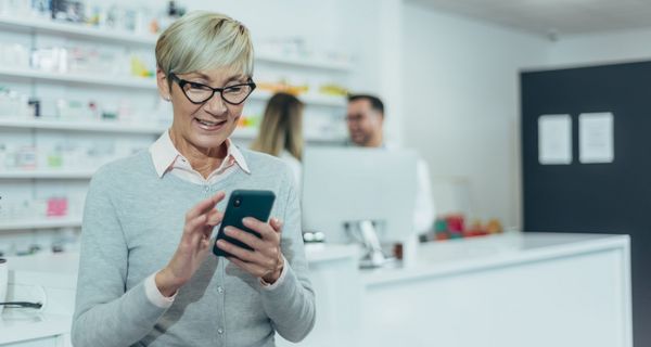 Seniorin mit ihrem Smartphone in der Apotheke.