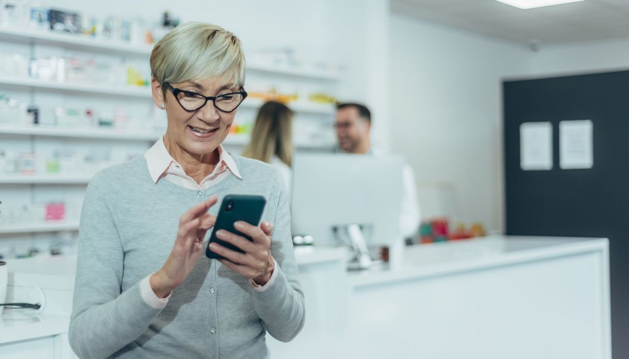 Seniorin mit ihrem Smartphone in der Apotheke.