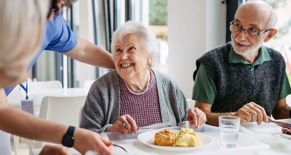 Eine ältere FRau und ein älterer Mann sitzen in einem esssahl und essen.