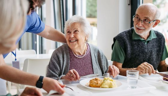 Eine ältere FRau und ein älterer Mann sitzen in einem esssahl und essen.