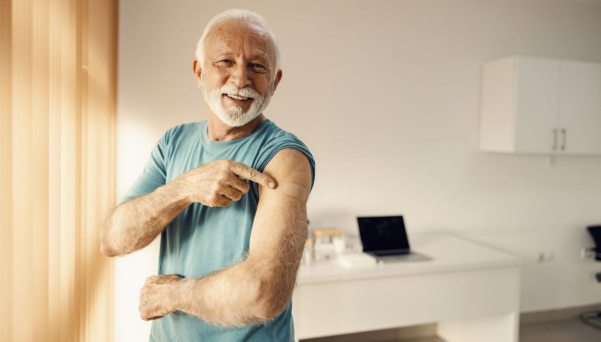 Mann, zeigt auf ein Pflaster auf seinem Arm.