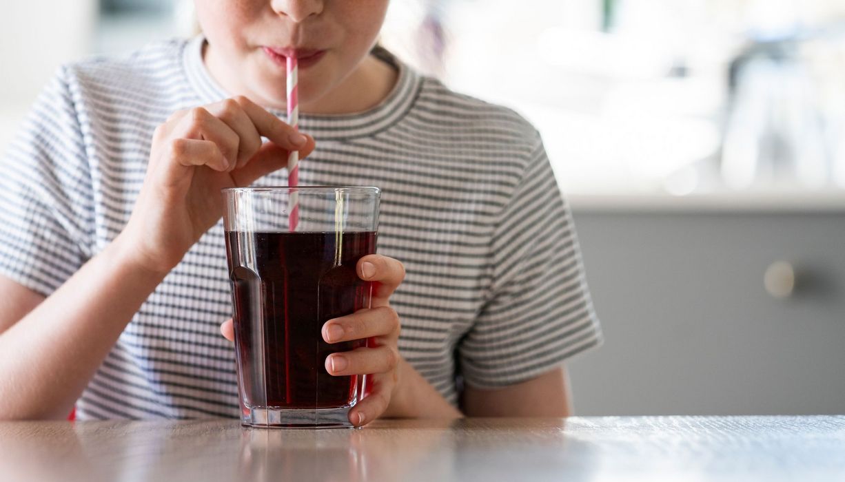 Frau, trinkt Cola aus einem Glas mit Strohhalm.