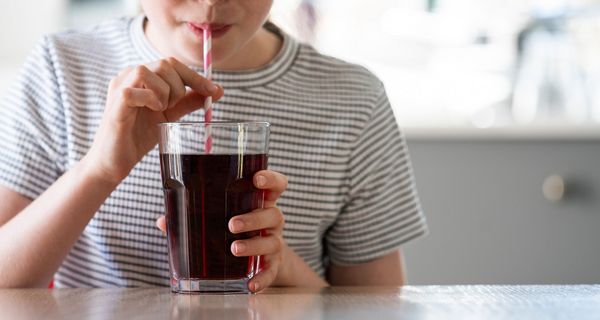 Frau, trinkt Cola aus einem Glas mit Strohhalm.