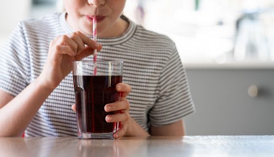 Frau, trinkt Cola aus einem Glas mit Strohhalm.