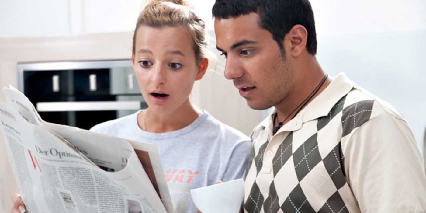 Junges Paar liest Zeitung mit entsetztem Gesichtsausdruck.