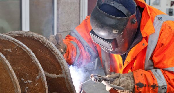 Arbeiter in orangefarbener Schutzkleidung und Schutzhelm mit Gesichtsschutz beim Schweißen