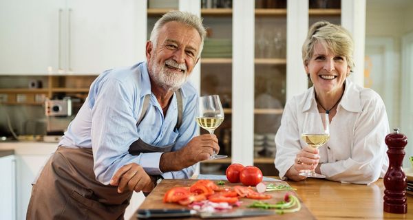 Senioren in der Küche, halten ein Glas Wein in der Hand.
