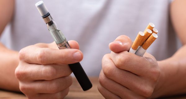 Eine Person hält in der einen Hand herkömmliche Zigaretten und in der anderen Hand eine E-Zigarette.