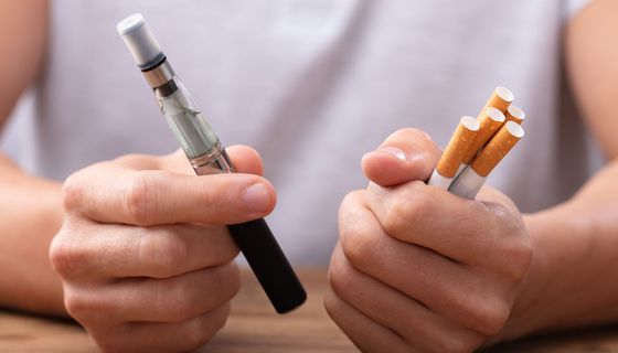 Eine Person hält in der einen Hand herkömmliche Zigaretten und in der anderen Hand eine E-Zigarette.