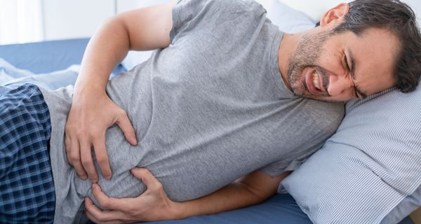 Mann krümmt sich vor Schmerzen auf dem Bett und hält sich den Bauch.