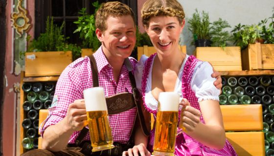 Paar in Trachten sitzt auf einer Bank und hält Biergläser in der Hand