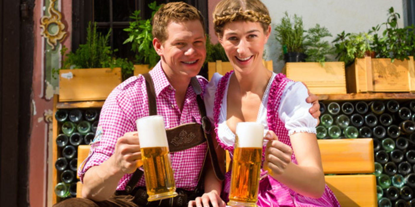 Paar in Trachten sitzt auf einer Bank und hält Biergläser in der Hand