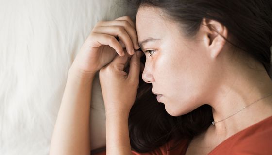 Junge Frau, liegt im Bett und starrt in die Luft.