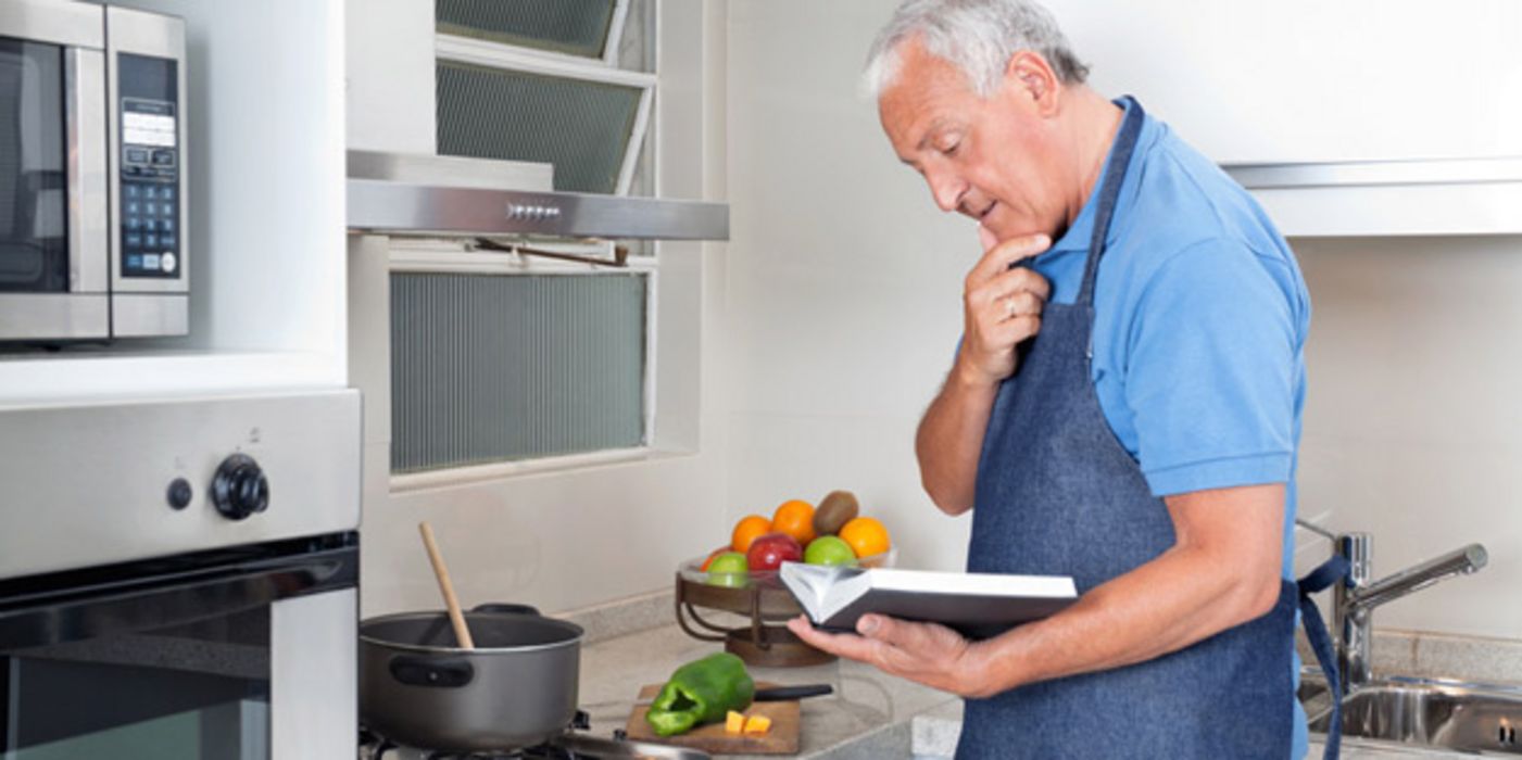 Älterer Mann studiert in der Küche ein Kochbuch