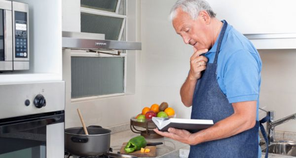 Älterer Mann studiert in der Küche ein Kochbuch
