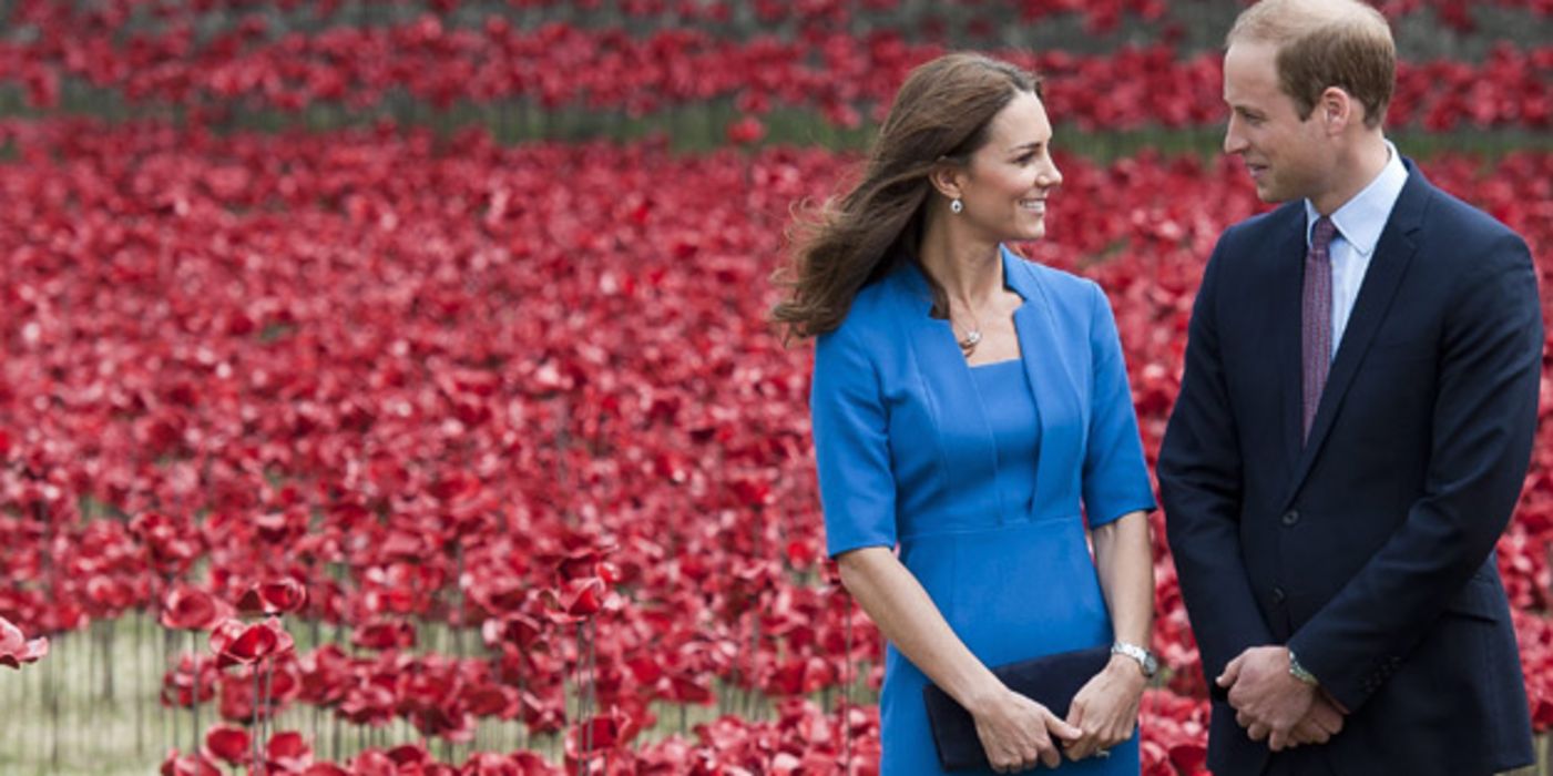 Herzogin Kate im himmelblauen Kleid und Prinz William schauen sich lächelnd in die Augen. Im Hintergrund ein Klatschmohnfeld (Installation in London)