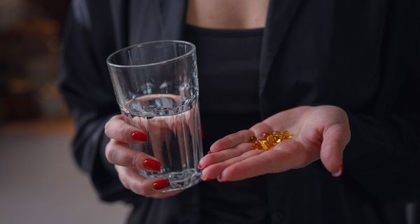 Frau, hält ein Glas Wasser und gelbe Kapseln in der Hand.