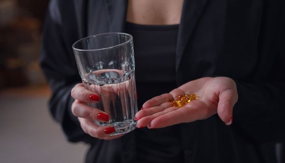 Frau, hält ein Glas Wasser und gelbe Kapseln in der Hand.