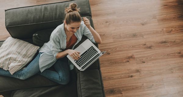 Junge Frau, sitzt mit Laptop auf der Couch.