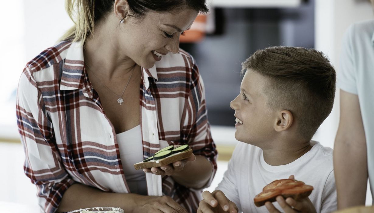 Frau schaut lächelnd auf einen Jungen herunter, beide halten vegetarisch belegte Brote in der Hand.