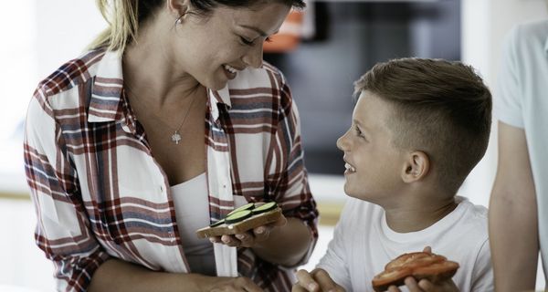 Frau schaut lächelnd auf einen Jungen herunter, beide halten vegetarisch belegte Brote in der Hand.