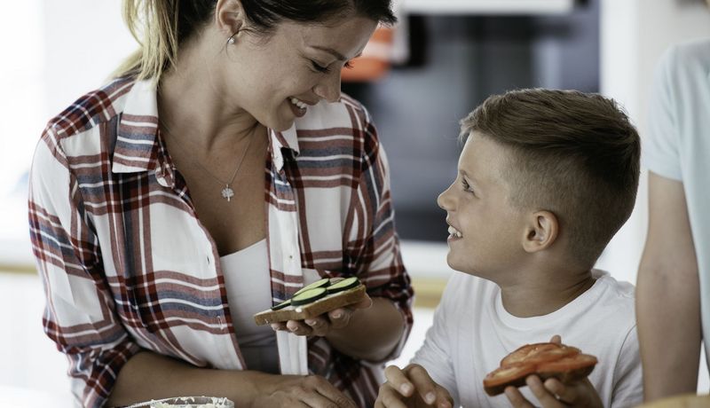 Frau schaut lächelnd auf einen Jungen herunter, beide halten vegetarisch belegte Brote in der Hand.
