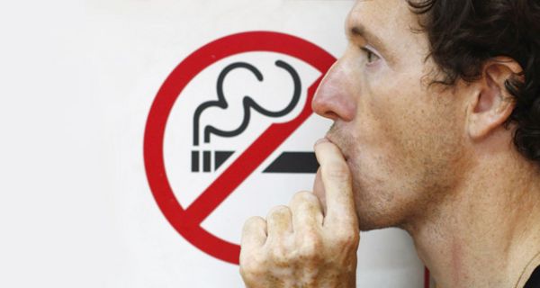 Mann mit Dreitagebart vor einem Rauchverbotsschild tut so als ob er rauchen würde