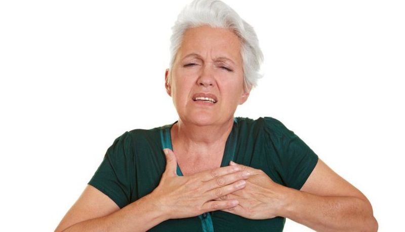 Ältere Frau mit schmerzverzerrtem Gesicht presst beide Hände auf die Brust