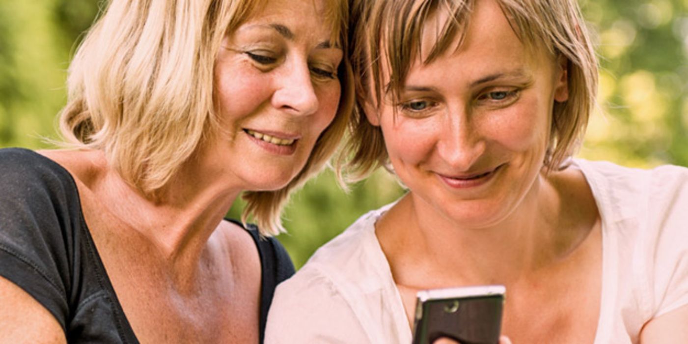 Zwei Frauen in der Natur schauen auf ein Smartphone