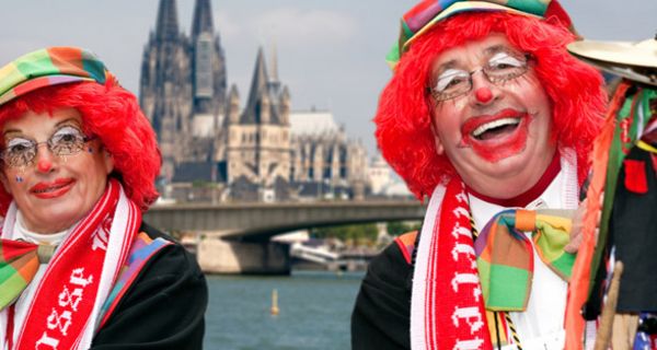 Karnevalistisches Paar in Clowsnsschminke und Hüten mit roten Perücken lackend vor Rhein und Kölner Dom