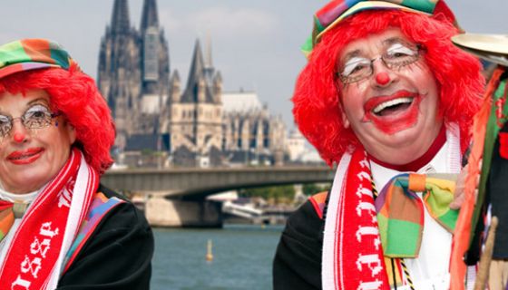 Karnevalistisches Paar in Clowsnsschminke und Hüten mit roten Perücken lackend vor Rhein und Kölner Dom